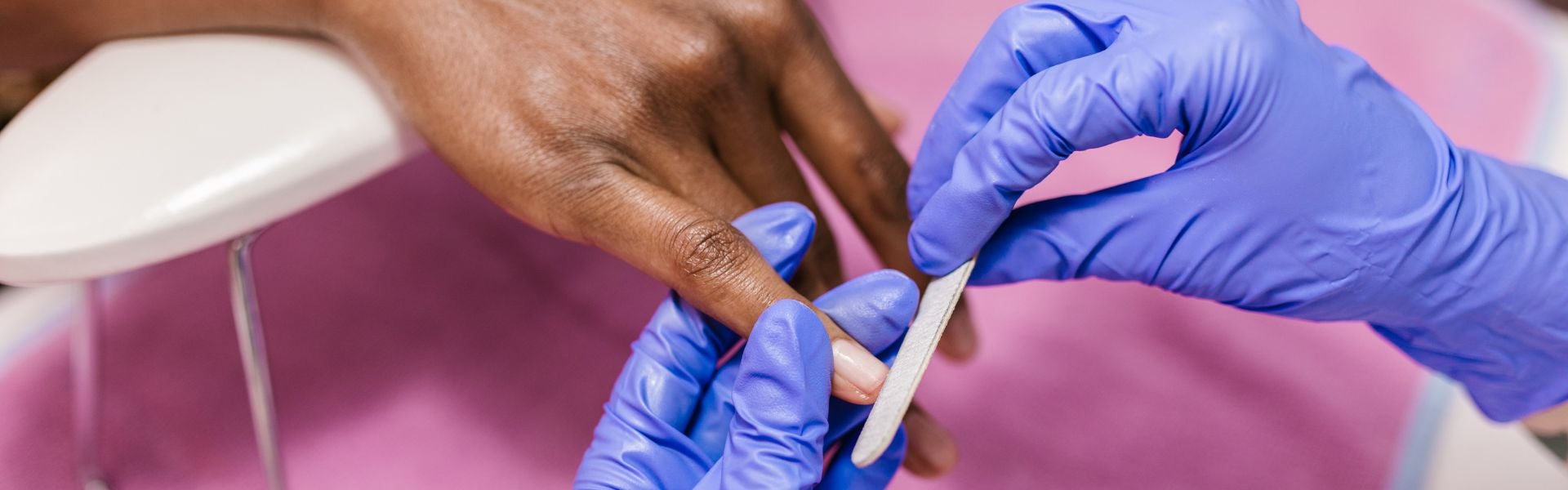 Mãos com luvas lixando unha de pessoa como preparação para alongamento. 