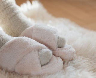 Sobre um tapete felpudo, pés usando meias e pantufas, simbolizando cuidados no inverno.
